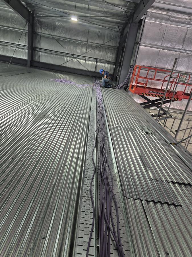 Trabajo en altura con plataforma elevadora sobre una bandeja portacables en nave industrial